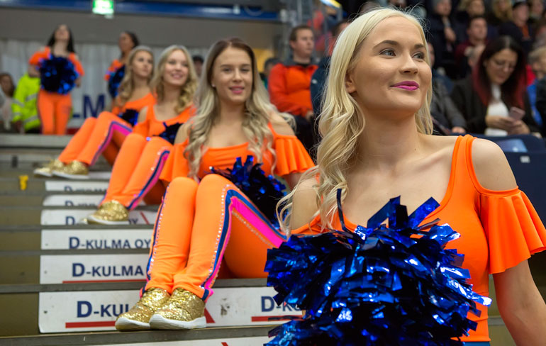 Ottelun ollessa käynnissä cheerleaderit istuskelevat hallin portailla.